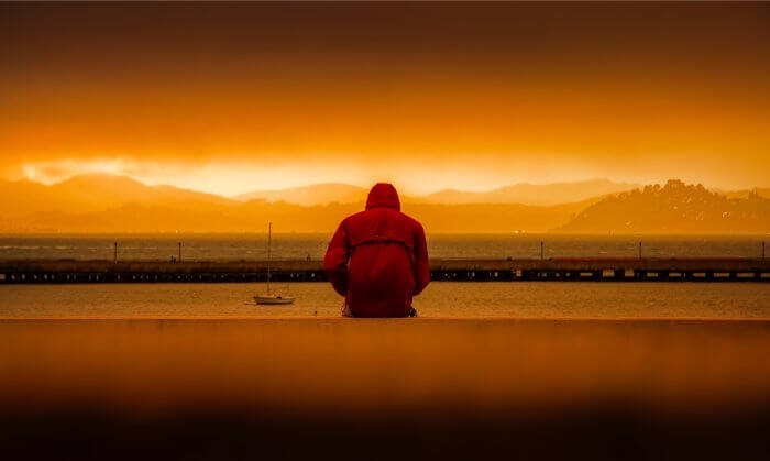 夕日の中海を見ている落ち込んだ男性の写真